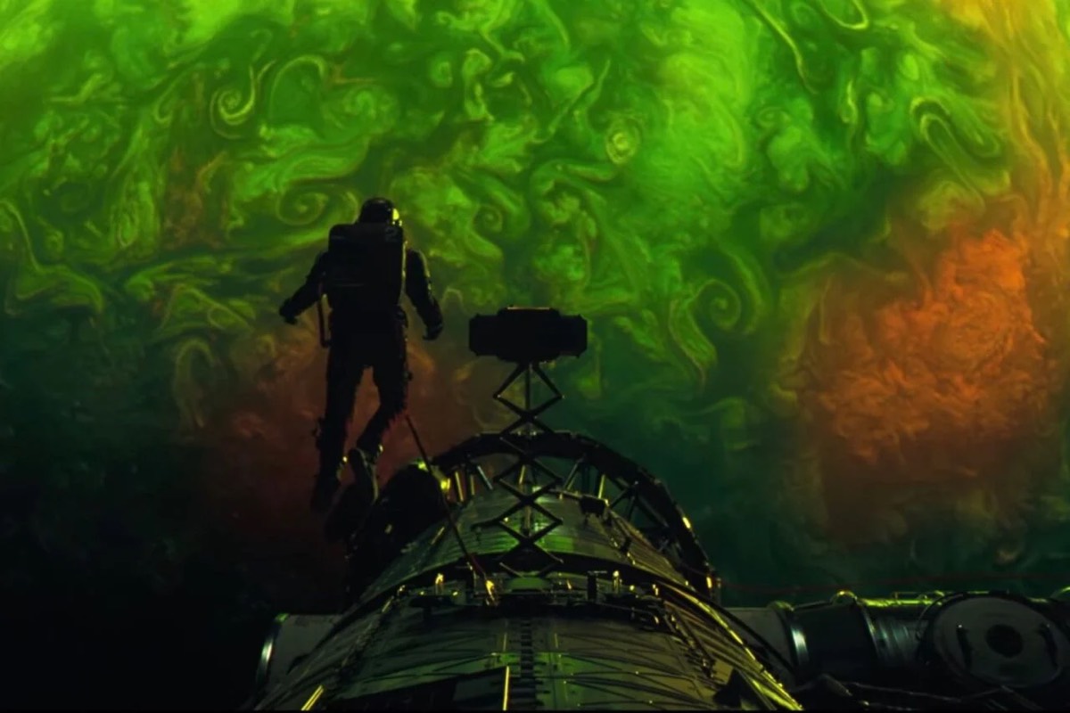 Ryan Gosling in a spacesuit in front of an alien planet of swirling green and red gases.
