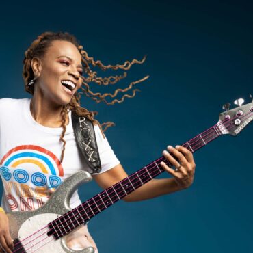 Photo of artist Divinity Roxx holding her bass guitar and smiling.